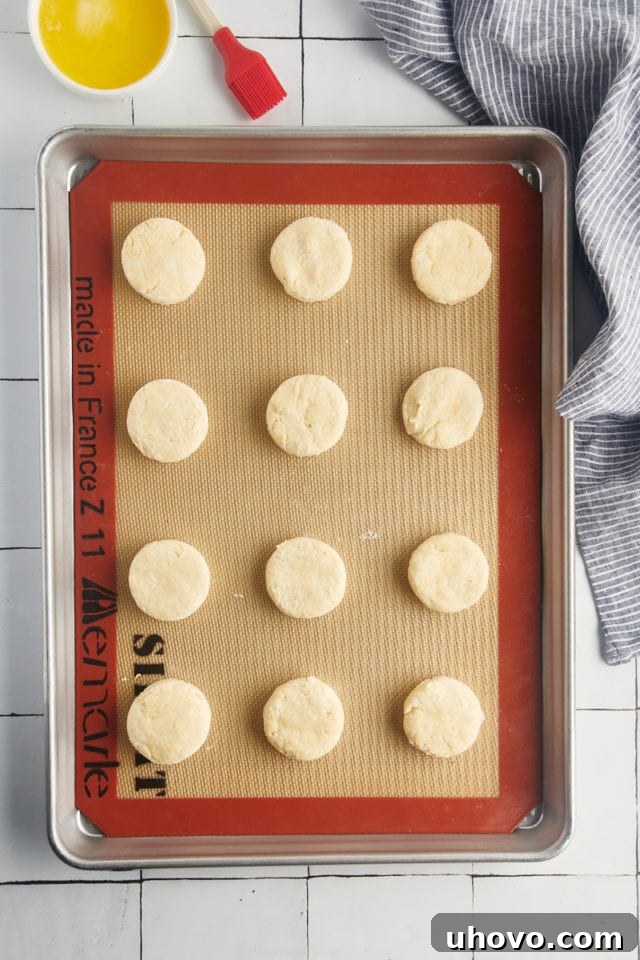 Overhead view of unbaked cream biscuits arranged on a Silpat-lined baking sheet.