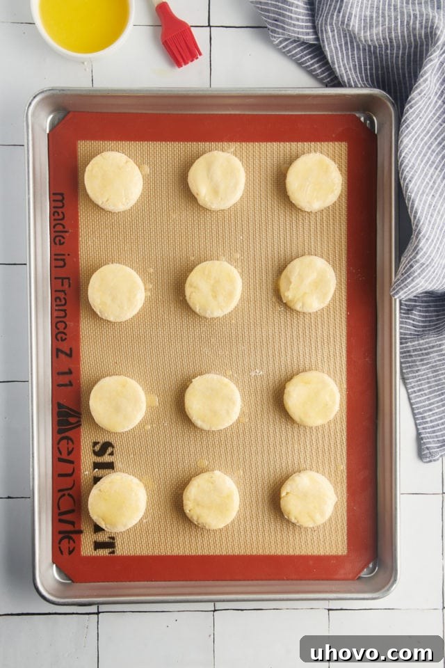 Overhead view of unbaked cream biscuits on a Silpat-lined baking sheet after being brushed with melted butter.