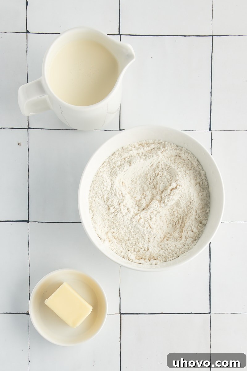 Overhead view of self-rising flour, heavy cream, and a stick of butter—the three simple ingredients for cream biscuits.