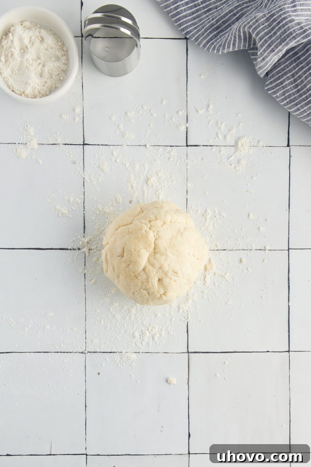 Overhead view of a shaggy ball of biscuit dough on a lightly floured countertop.