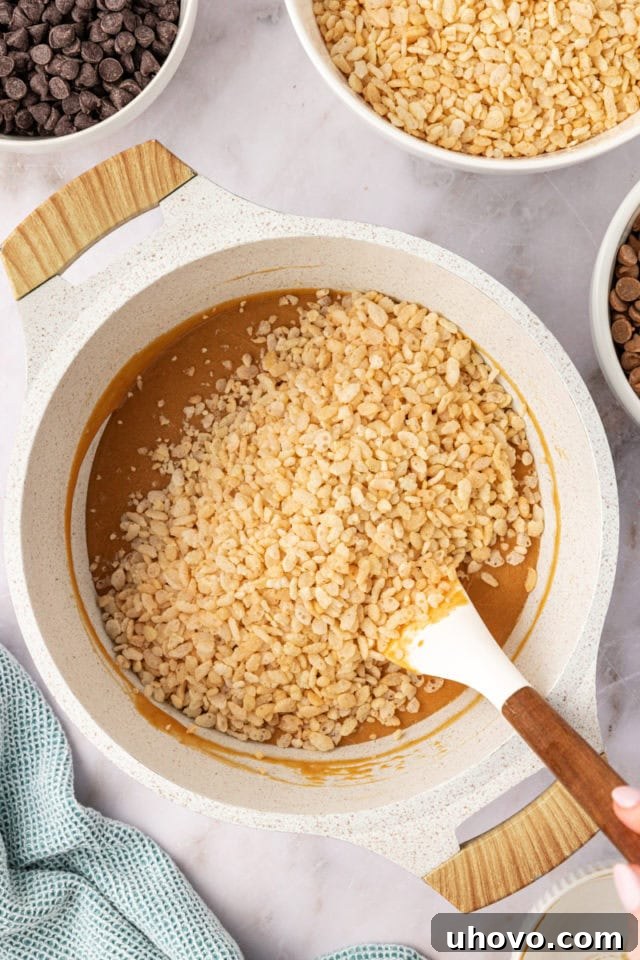 Crisp rice cereal being gently folded into the warm, peanut butter-infused mixture in a large bowl, ensuring every piece is thoroughly coated.