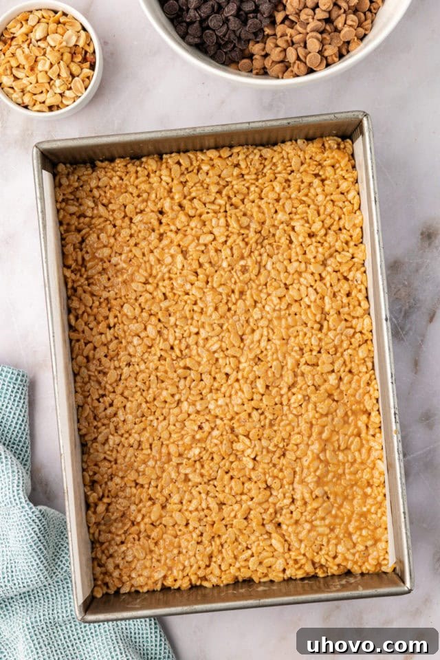 An overhead perspective of the peanut butter rice crispy treat mixture evenly pressed into a 9x13 inch pan, forming the sturdy base for the decadent topping.