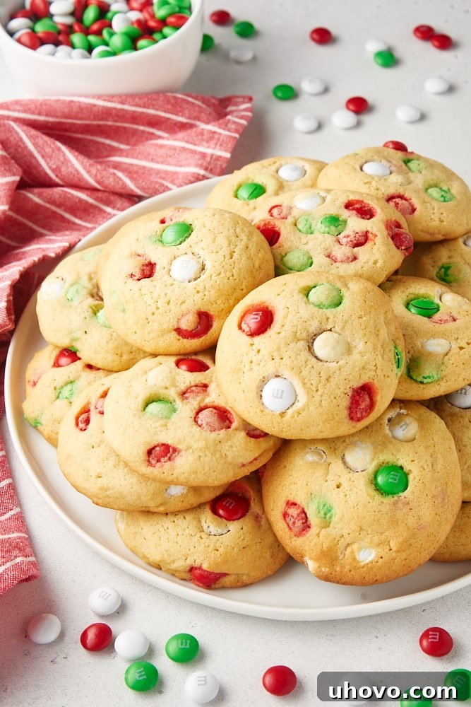 Christmas M&M cookies piled on a white plate with M&Ms scattered around the plate.