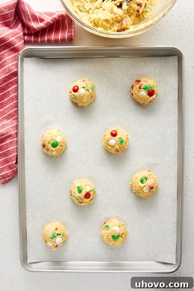 Overhead view of M&M cookie dough portioned and placed on a parchment-lined baking sheet.