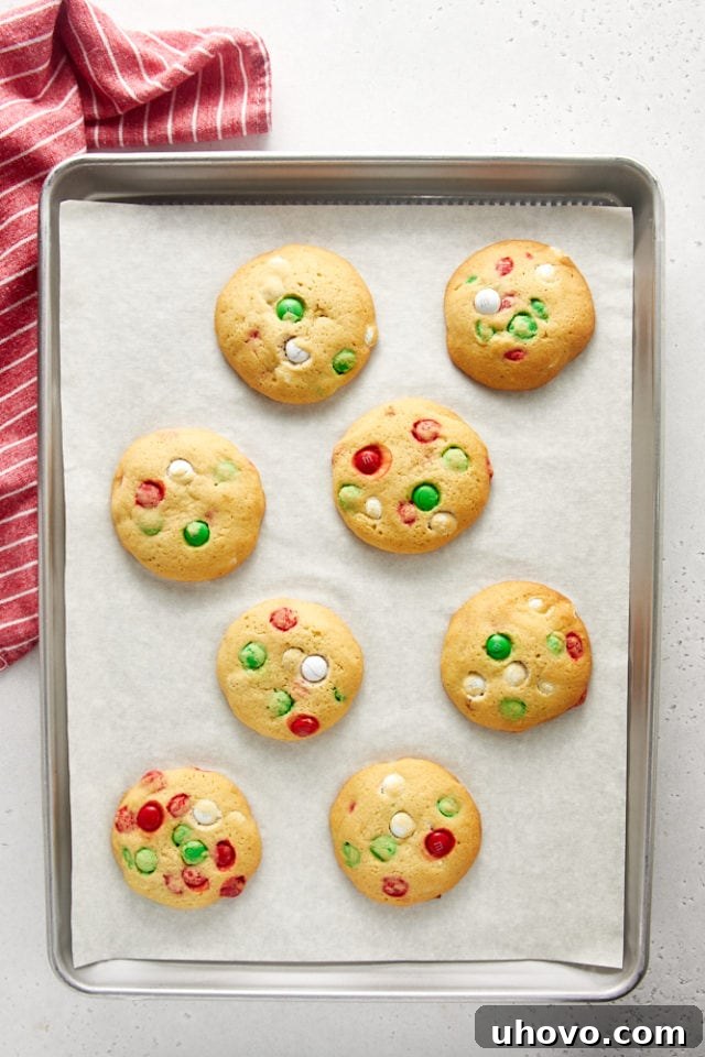 Overhead view of freshly baked Christmas M&M cookies on a parchment-lined baking sheet.