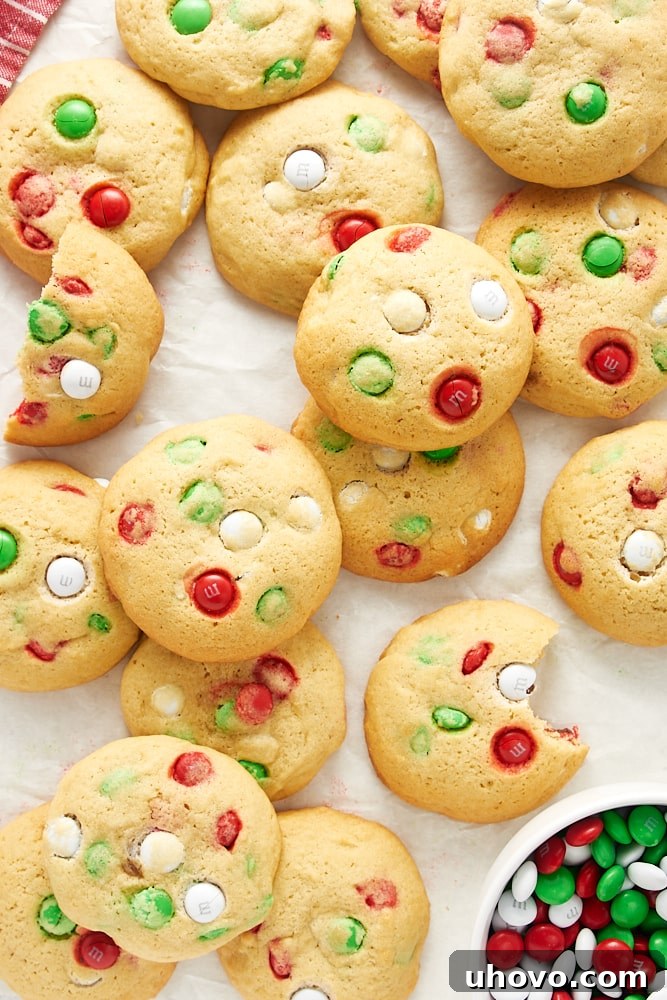 Overhead view of Christmas M&M cookies scattered and piled on white parchment paper.