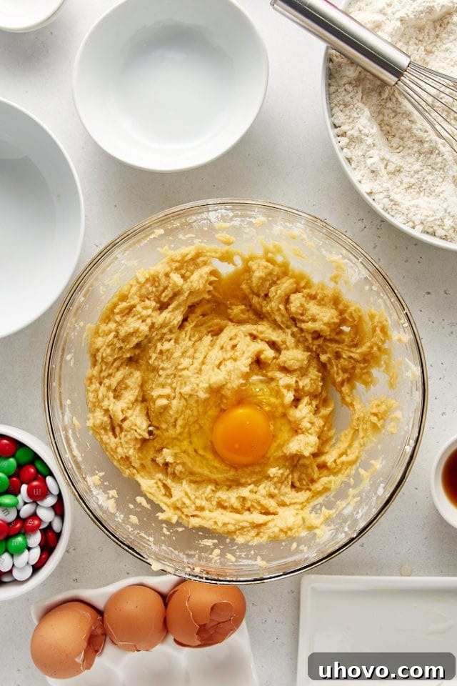 Overhead view of egg added to cookie dough in a glass mixing bowl.