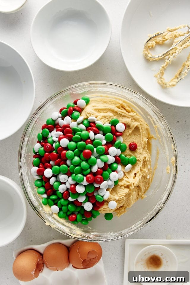 Overhead view of Christmas M&Ms added to cookie dough in a glass mixing bowl.