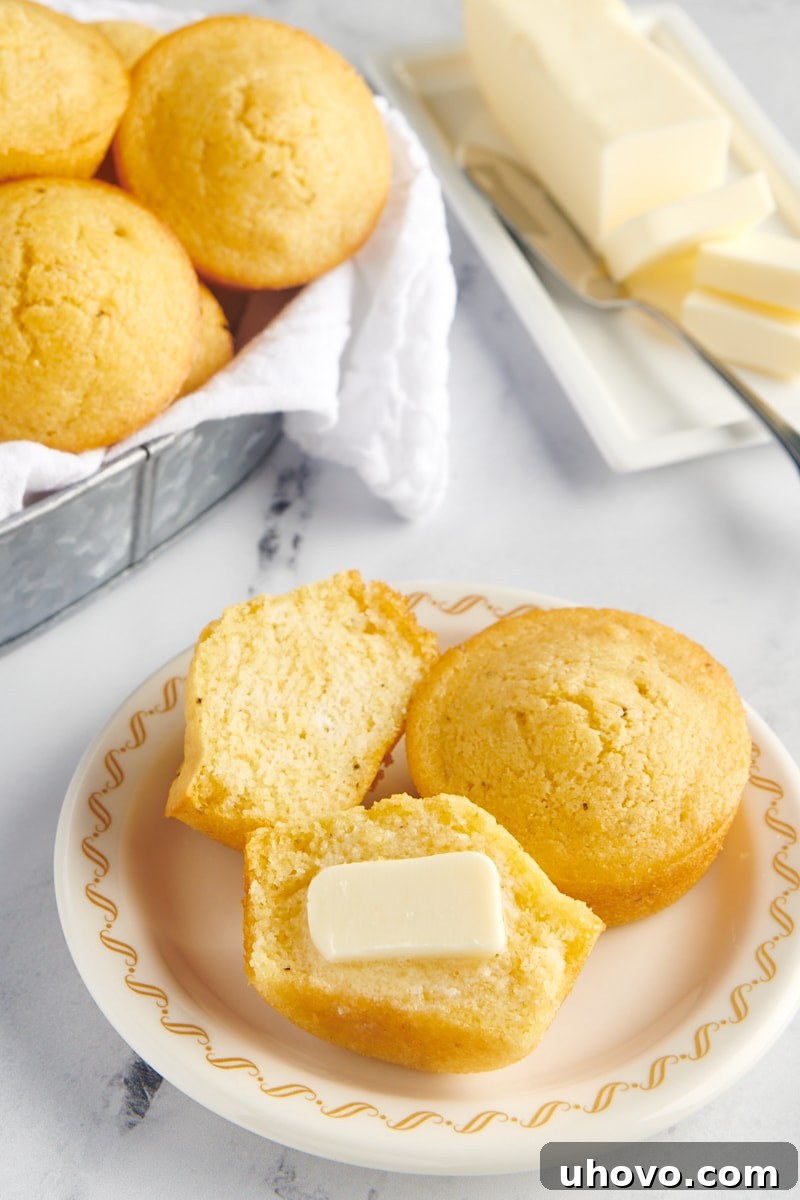 A freshly baked corn muffin, expertly sliced in half, revealing its tender, moist interior, with a generous pat of butter melting invitingly on top.