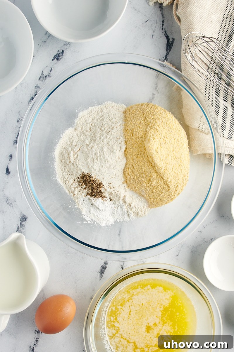 Separate glass mixing bowls showcasing dry ingredients (flour, cornmeal) and wet ingredients (melted butter, egg) for corn muffins.