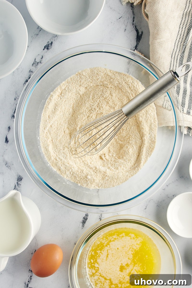 A glass mixing bowl containing perfectly combined dry ingredients for corn muffins, including flour, cornmeal, baking powder, salt, and pepper.