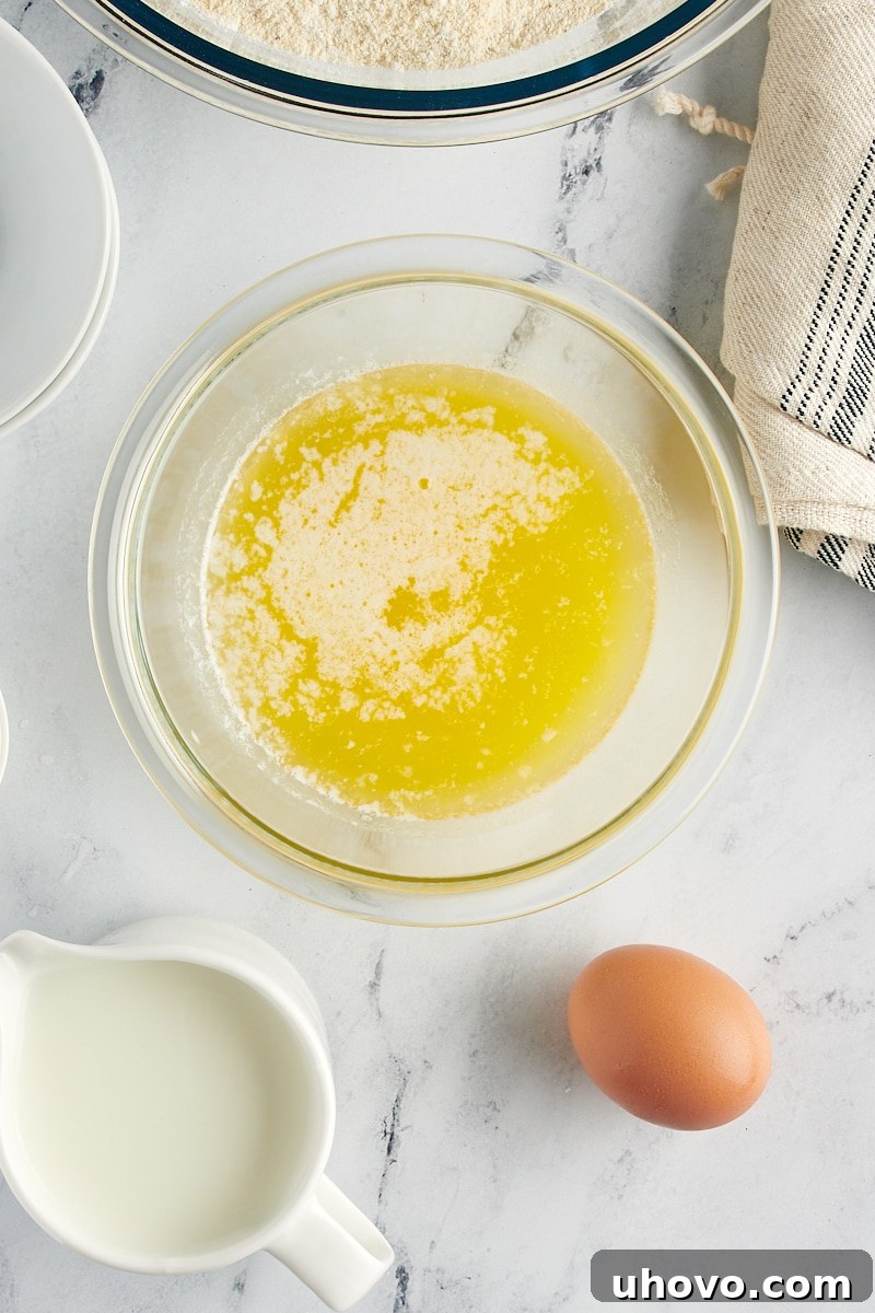 A small glass bowl holding golden melted butter, positioned beside a fresh raw egg, both at the ideal temperature for mixing.