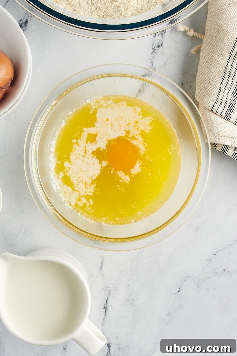 A hand gently cracking a room-temperature egg into a bowl of slightly cooled melted butter, preparing the wet ingredients for corn muffins.