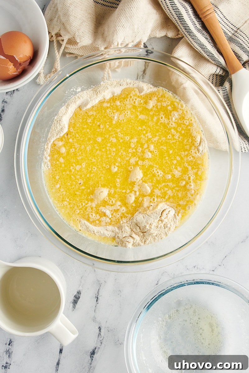 The smooth, liquid wet ingredients being poured carefully into the larger bowl containing the dry flour and cornmeal mixture.