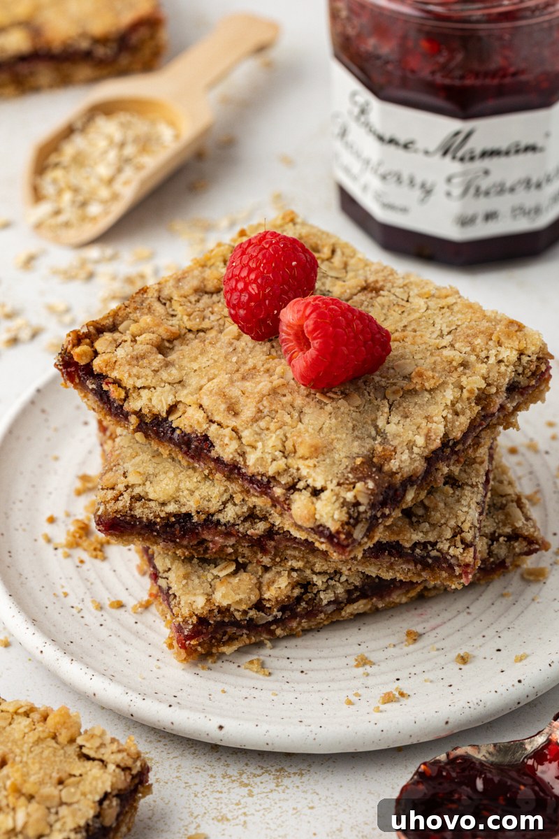 three raspberry oatmeal bars stacked on a white plate and topped with two fresh raspberries