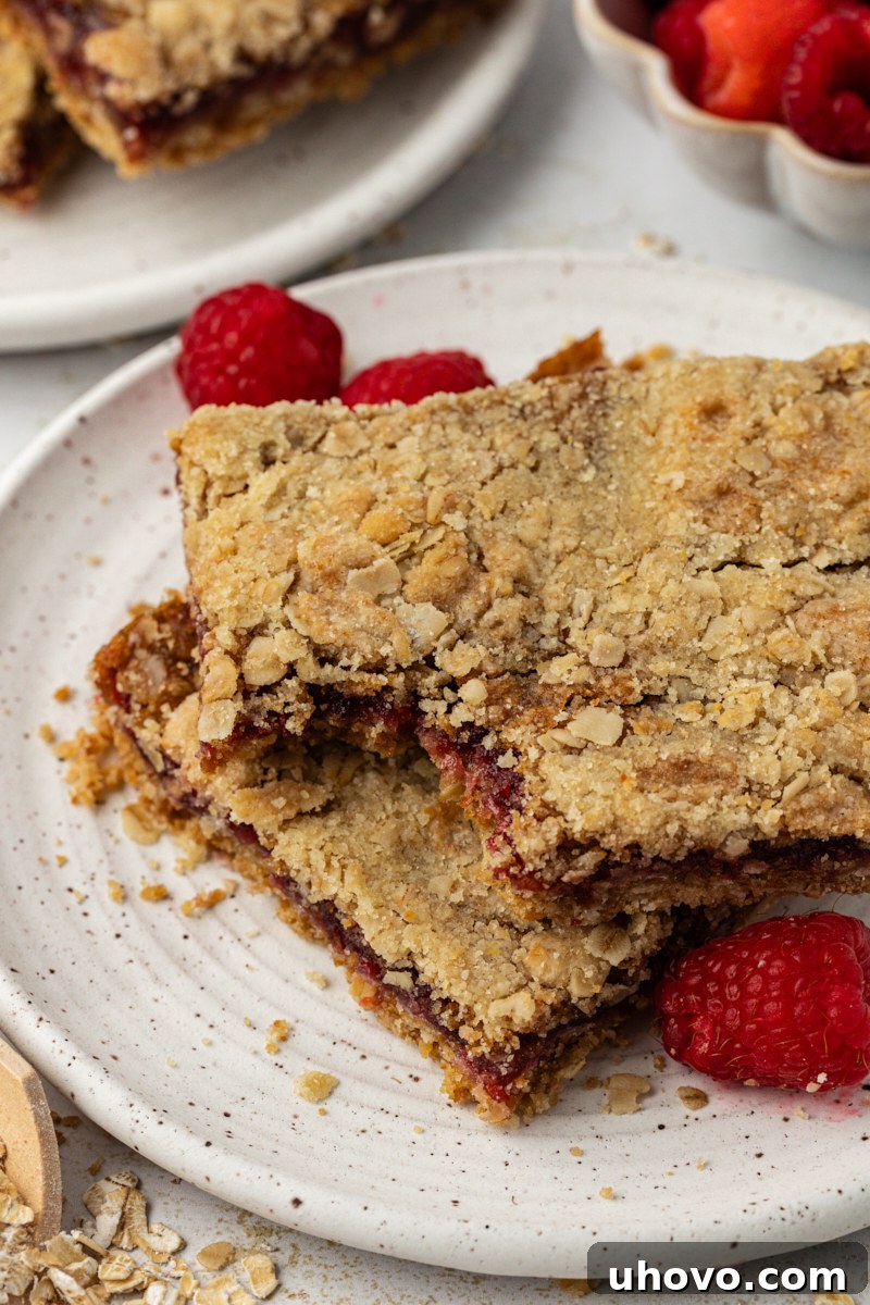 a raspberry oatmeal bar with a bite missing stacked on top of another bar on a white plate