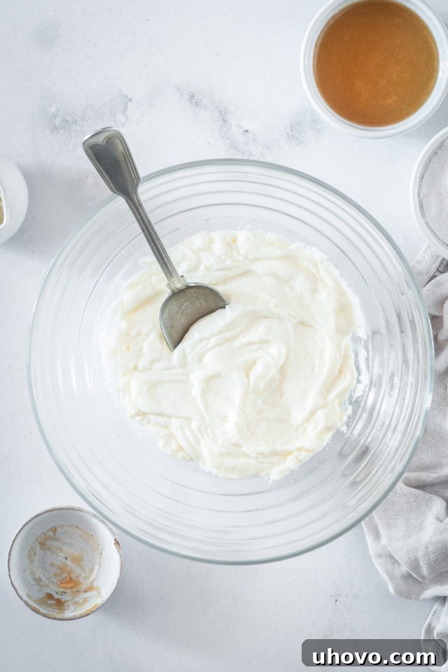 An overhead shot showing softened butter and cream cheese being beaten together in a clear glass bowl with an electric mixer, forming the creamy base for the caramel cream cheese frosting.