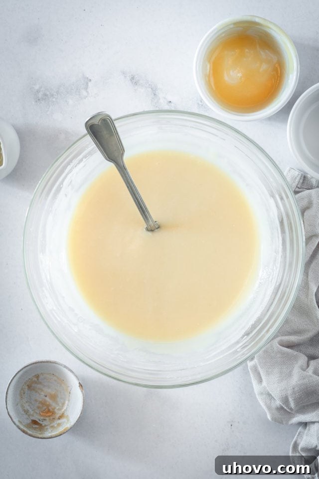 An overhead shot of rich, smooth caramel cream cheese frosting in a clear glass mixing bowl, after all ingredients have been incorporated, showing its inviting texture and golden hue.