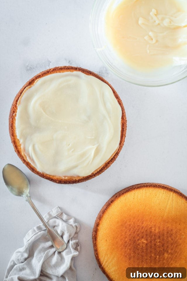 An overhead shot illustrating the assembly of the Southern caramel cake layers, with the first layer frosted over the caramel, and the second cake layer being placed on top, ready for final frosting.