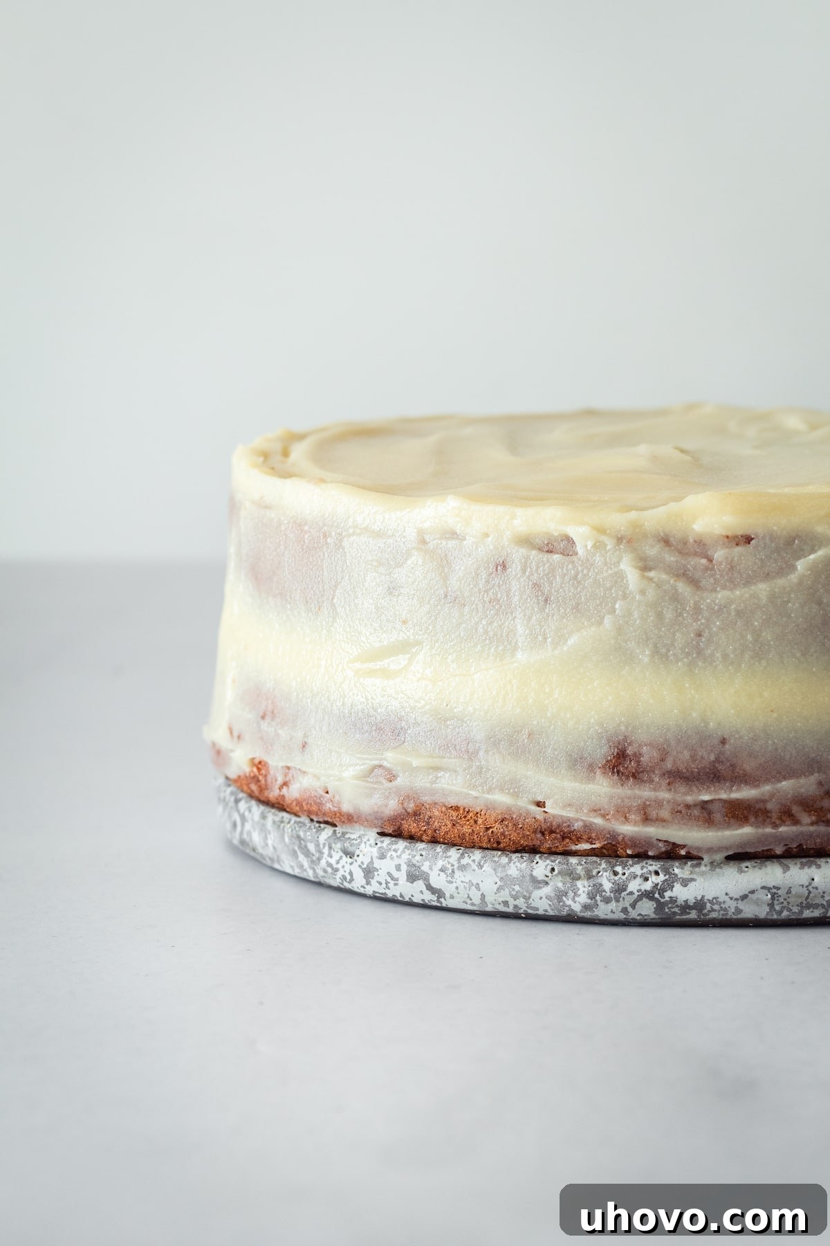 A stunning, fully frosted caramel cake standing proudly on a decorative cake plate, showcasing its smooth caramel cream cheese frosting and inviting texture, ready for any occasion.