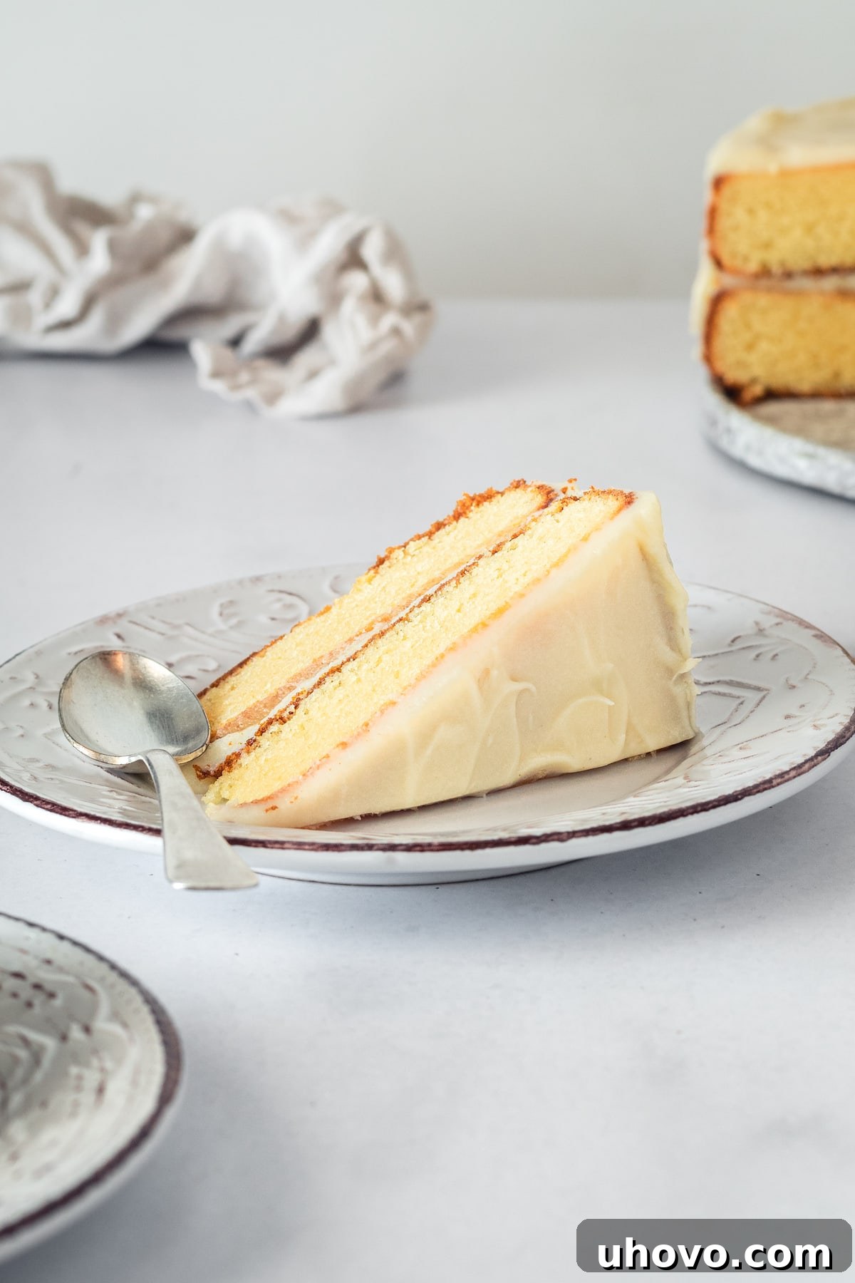A pristine slice of caramel cake, expertly frosted with caramel cream cheese and resting on a white plate, showcasing its impeccable layers and inviting texture for a perfect dessert moment.
