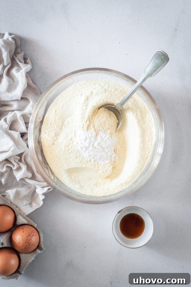 An overhead shot of dry caramel cake ingredients, including flour, baking powder, and salt, resting in a clear glass mixing bowl, ready to be combined for the cake batter.