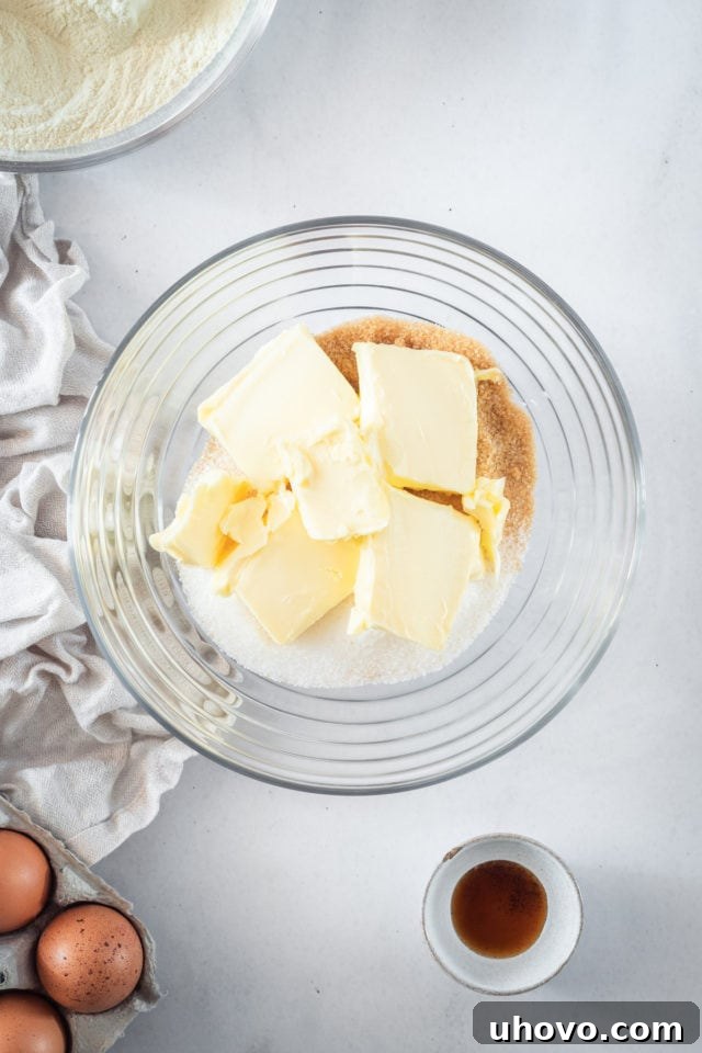 An overhead shot of softened butter and two types of sugar (granulated and light brown) in a clear glass bowl, being creamed together to form the base of the caramel cake batter.