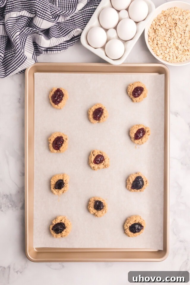 overhead view of oatmeal thumbprint cookies on a parchment-lined baking sheet ready to go into the oven