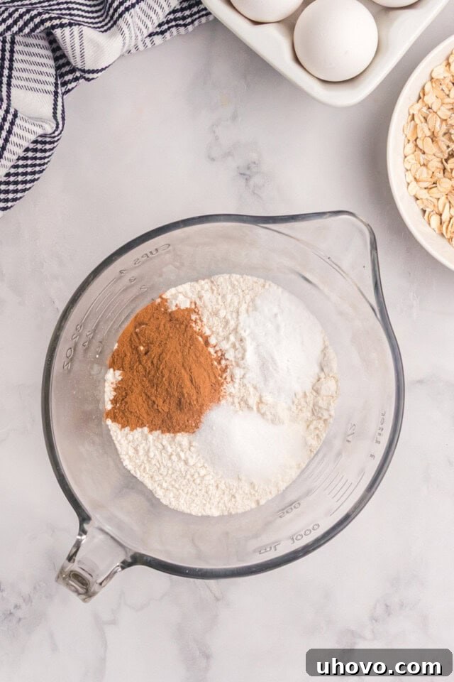 overhead view of flour, baking soda, cinnamon, and salt in a glass mixing bowl