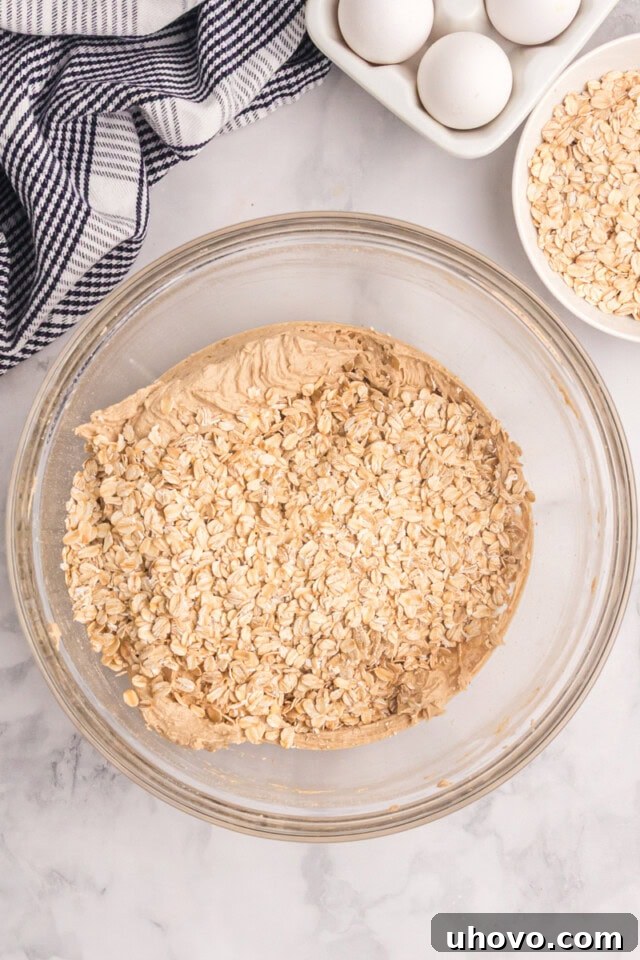 overhead view of oats added to cookie dough in a glass mixing bowl