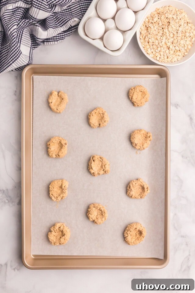 overhead view of oatmeal thumbprint cookies shaped on a lined baking sheet
