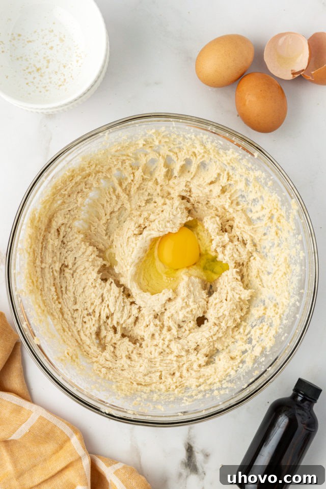 overhead view of an egg added to creamed butter and sugar in a white mixing bowl
