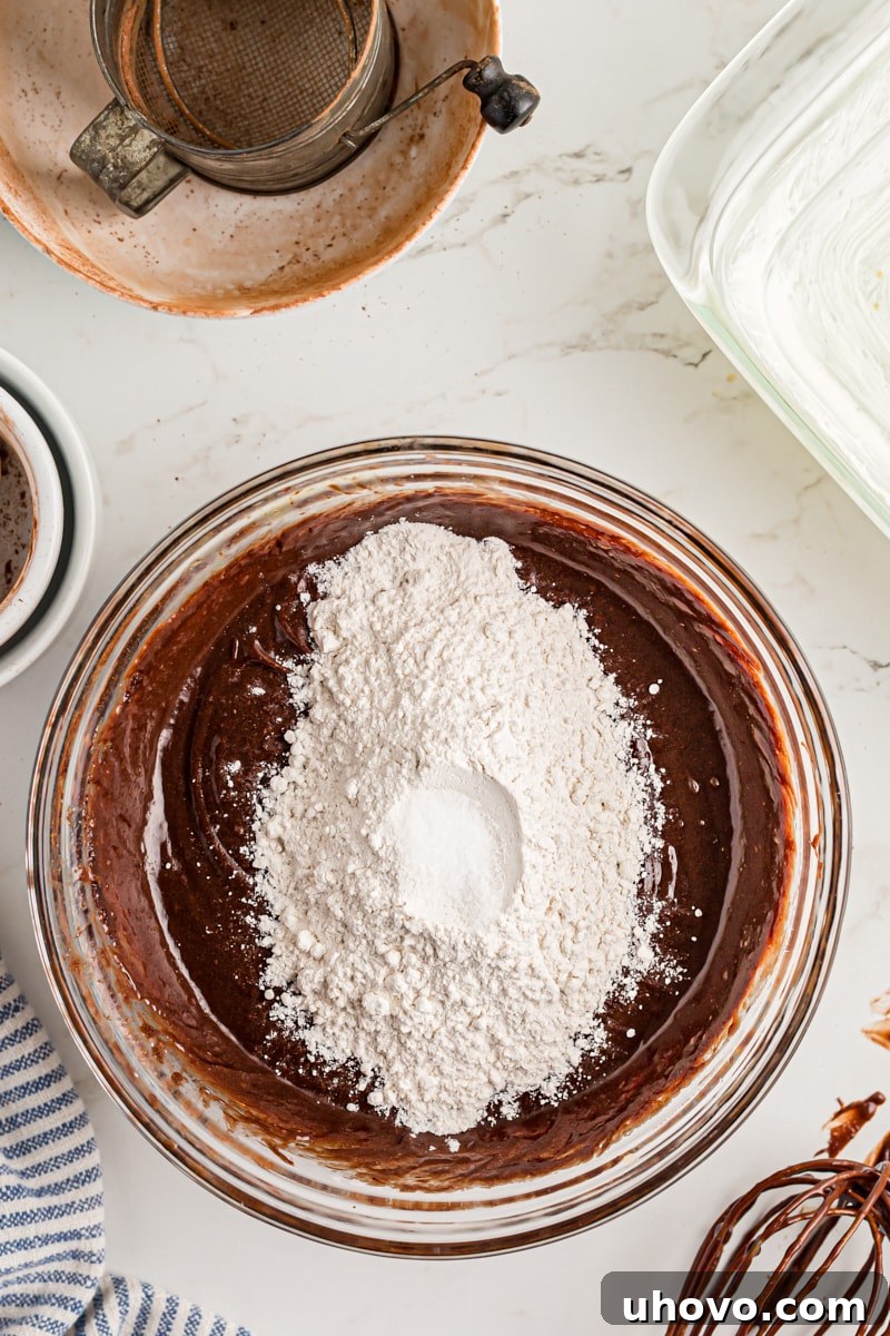 Overhead view of all-purpose flour and salt being folded into the wet ingredients for the brownies.