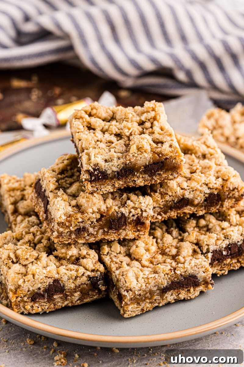 A stack of beautifully baked caramel oatmeal bars on a white plate, showcasing their inviting golden-brown crust and gooey center.