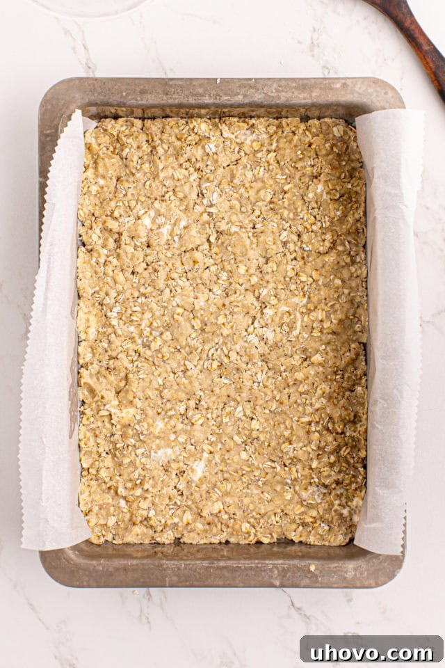 Oatmeal bar crust pressed into a baking pan, ready for its initial bake.