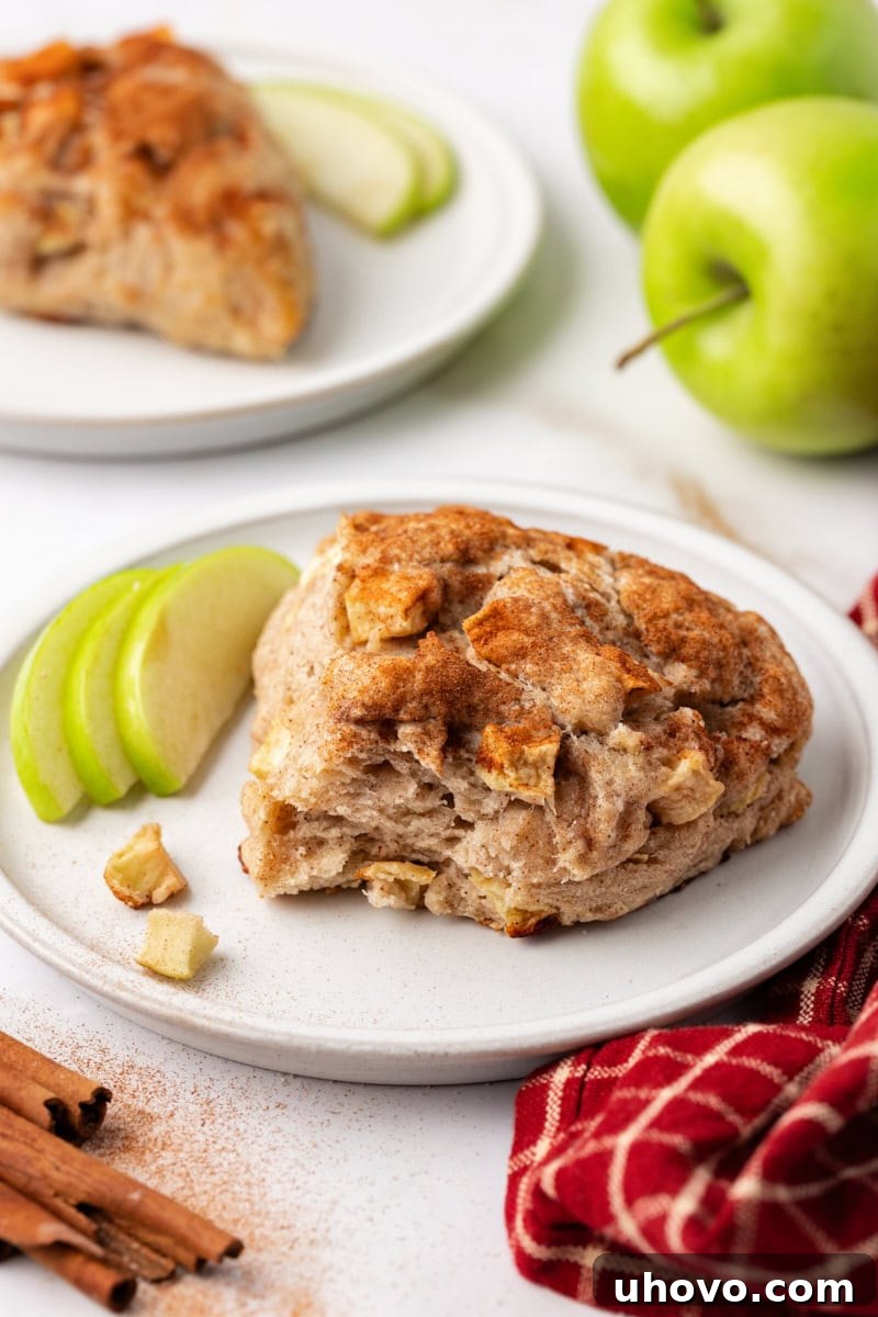 Tender apple cinnamon scones presented on a white plate with fresh apples in the background.