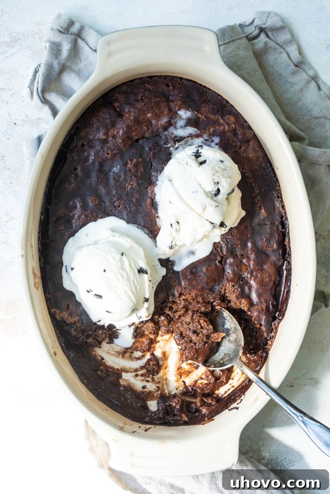 Rich Brownie Chocolate Pudding Cake in a baking dish, topped with generous scoops of vanilla ice cream, perfectly ready to be served warm.