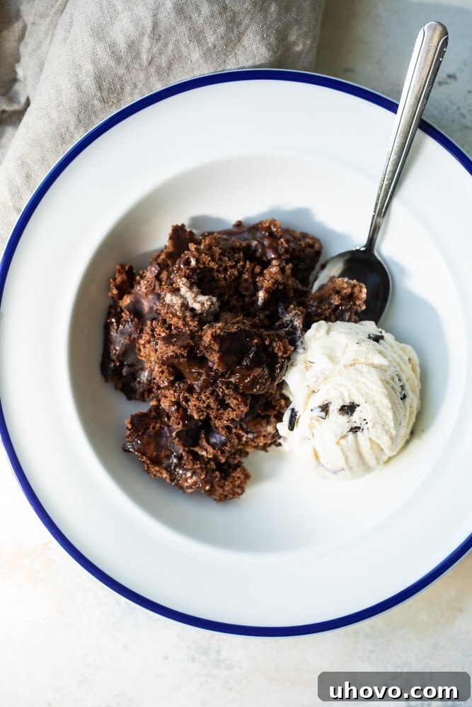 An inviting overhead shot of a freshly baked Brownie Chocolate Pudding Cake, nestled in a blue-rimmed white bowl, with steam gently rising, showcasing its warmth and gooey texture.