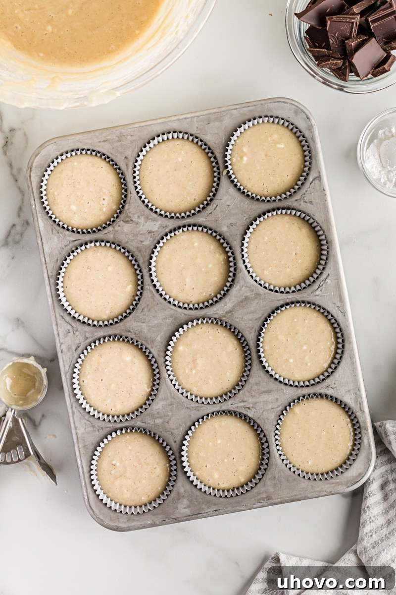Overhead view of cupcake batter scooped into paper-lined muffin cups in a baking pan.