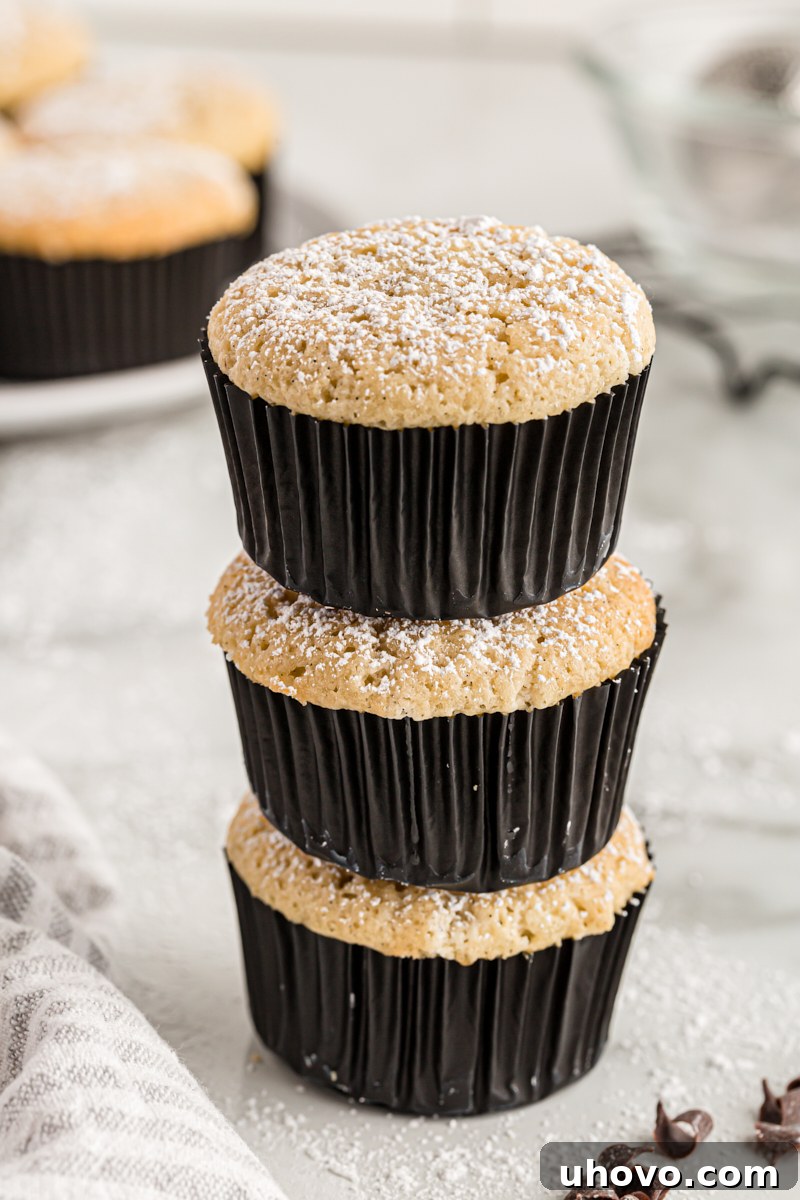 A stack of three perfectly baked vanilla chocolate-filled cupcakes, dusted with powdered sugar, highlighting their simple elegance.