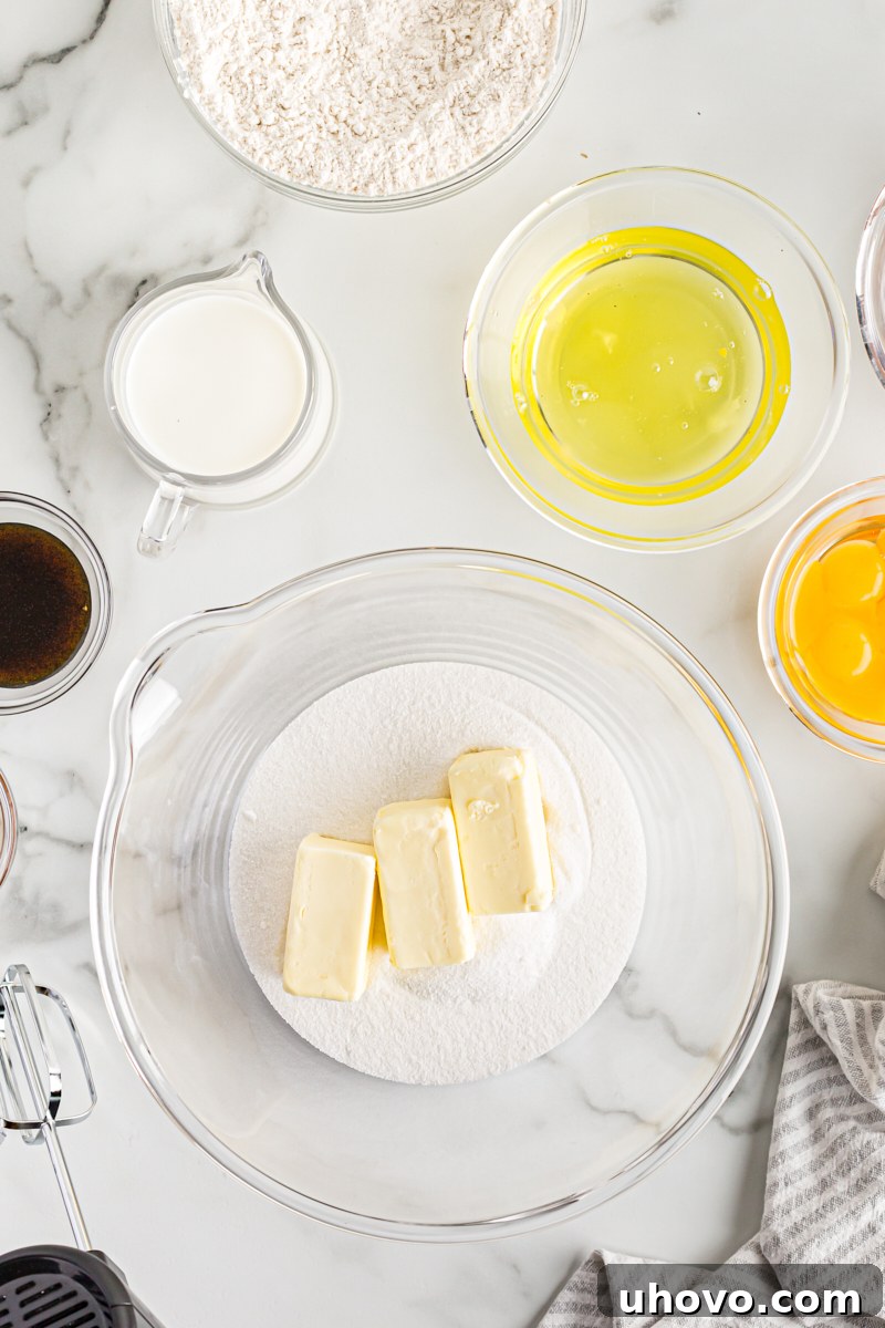 Overhead view of softened butter and granulated sugar in a clear glass mixing bowl, ready to be creamed.