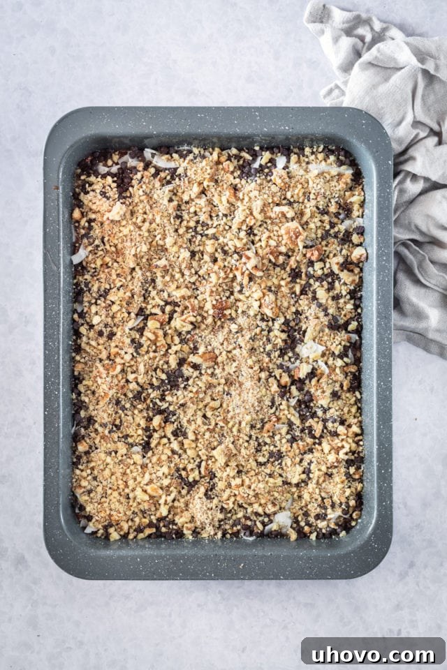 overhead view of coconut, chocolate chips, and finely chopped pecans generously sprinkled over the brownie batter in a rectangular baking pan