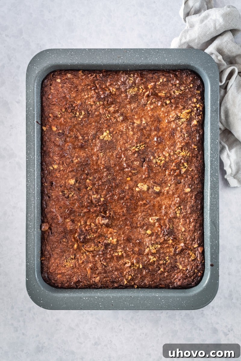 Overhead view of freshly baked caramel coconut pecan brownies cooling in a rectangular baking pan, with a golden-brown, inviting top layer.