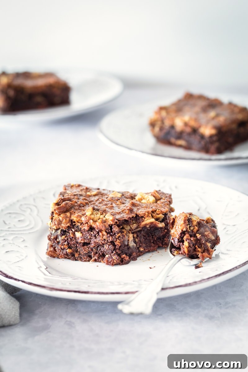 A perfectly portioned caramel coconut pecan brownie presented on a white plate, with a bite taken and a fork resting beside it, highlighting its tempting layers.