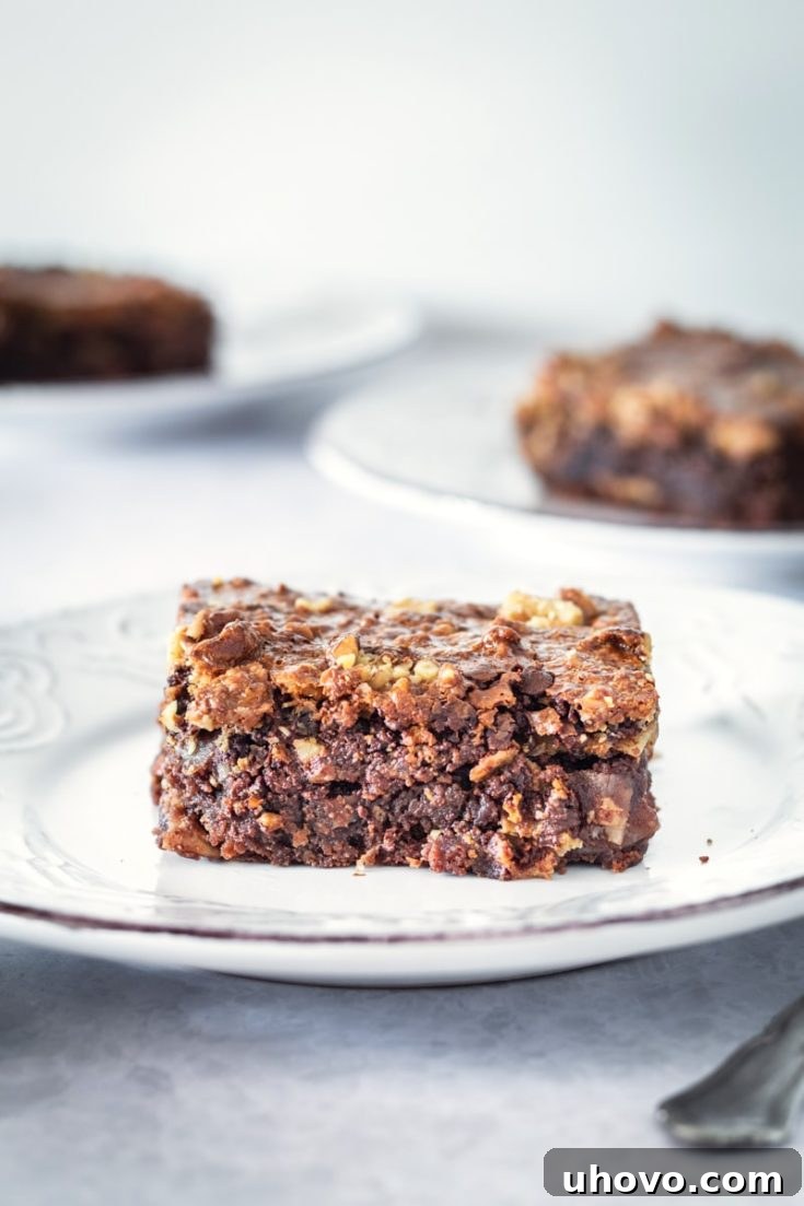 a Caramel Coconut Pecan Brownie on a white plate with more brownies in the background, showcasing its rich, layered texture