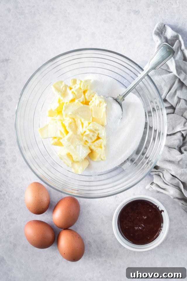 overhead view of softened butter and granulated sugar combined in a clear glass mixing bowl, ready for beating