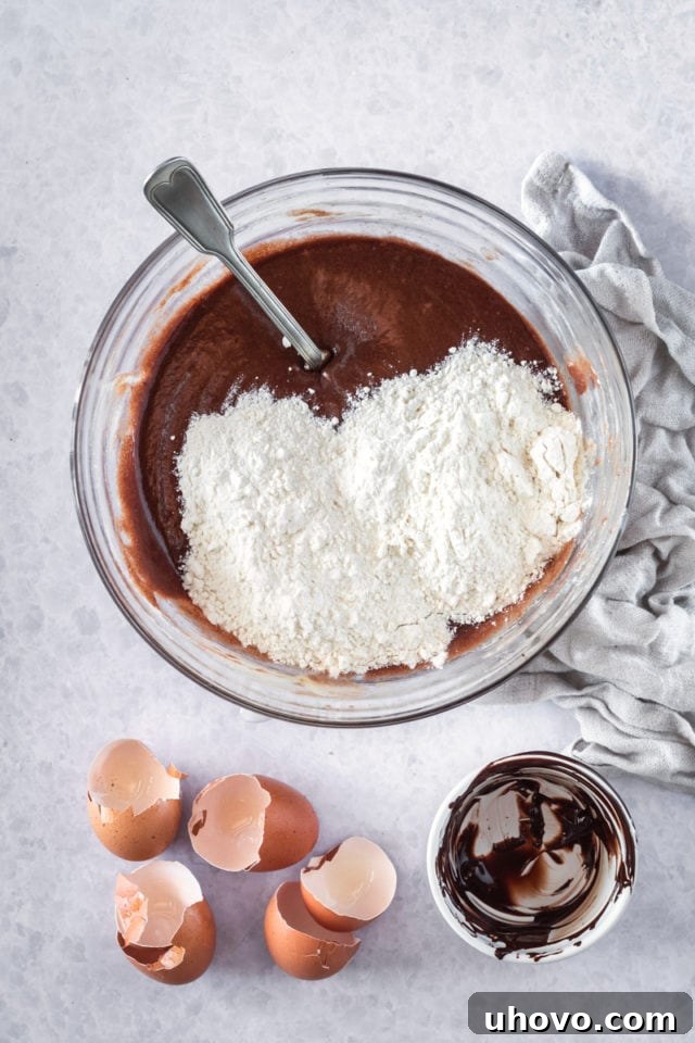 overhead view of all-purpose flour being gently added to the brownie batter in a glass mixing bowl