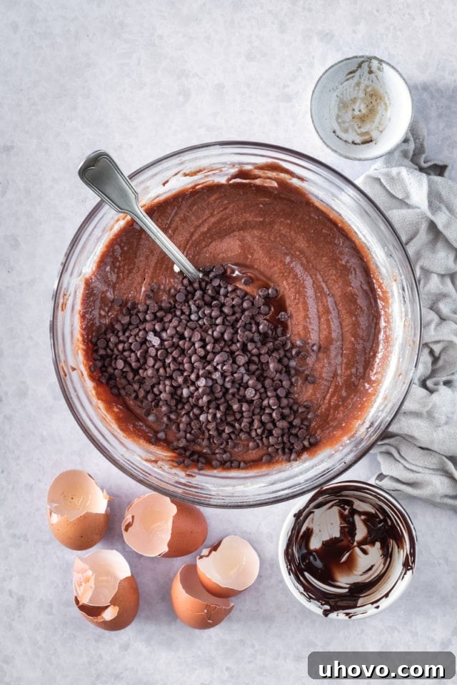 overhead view of semisweet chocolate chips being carefully stirred into the rich brownie batter in a glass mixing bowl