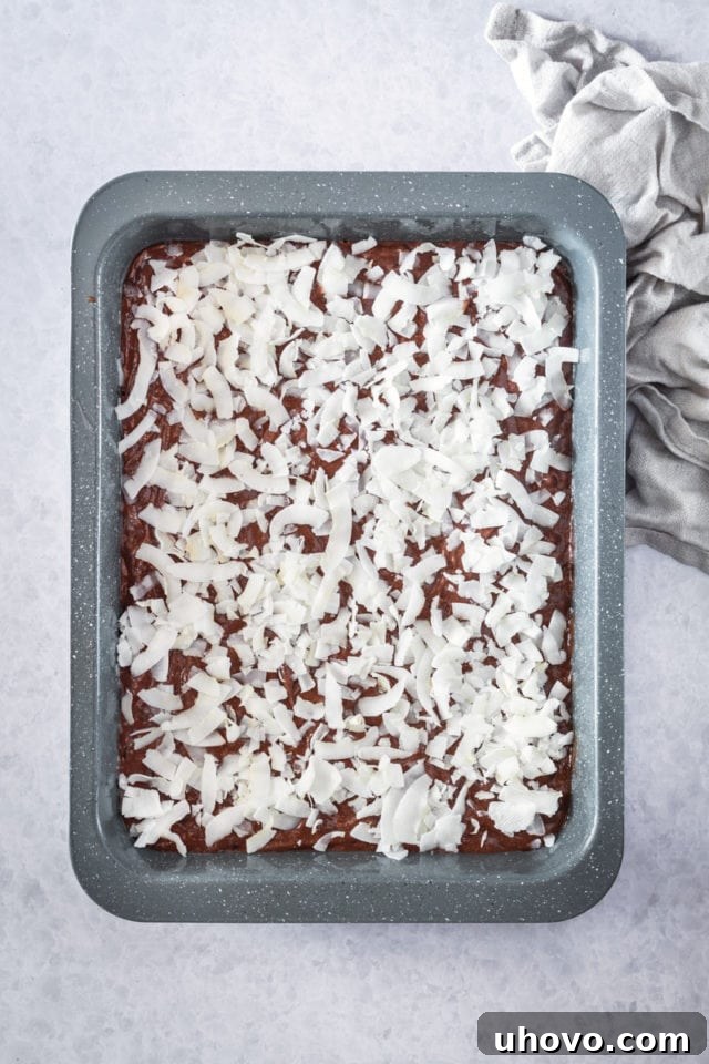 overhead view of sweetened flaked coconut generously sprinkled over the rich brownie batter in a rectangular baking pan