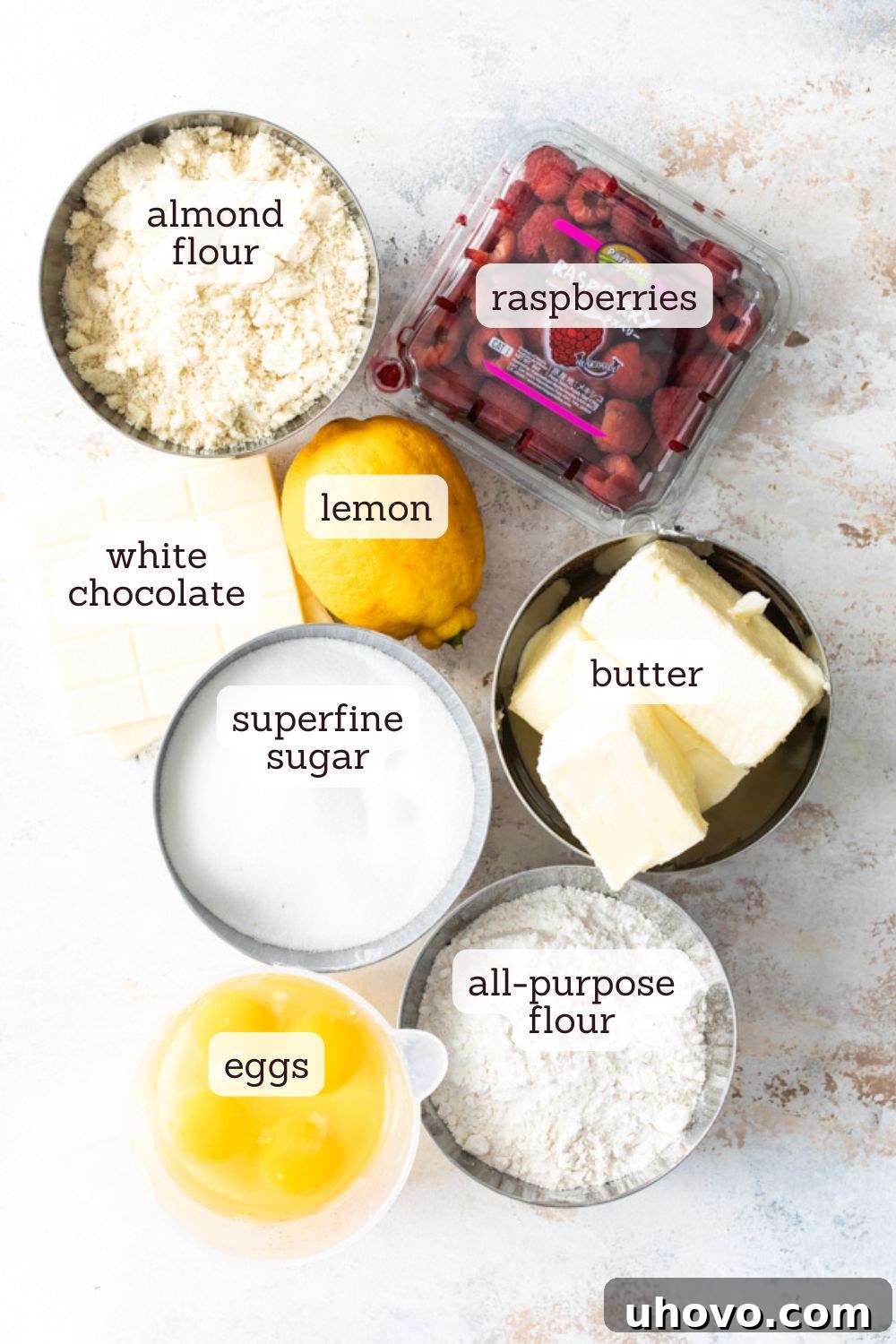 Overhead view of various ingredients for raspberry white chocolate almond loaf laid out on a clean white surface.